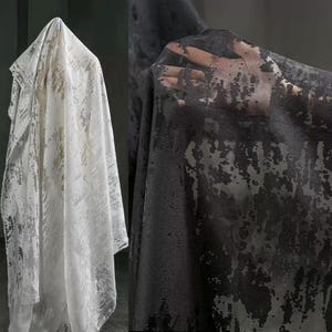 Puede incluir: Dos piezas de tela, una blanca y otra negra, con un patrón texturizado y abstracto. La tela blanca está drapeada, revelando la textura. La tela negra se sostiene, mostrando el patrón y la transparencia del material.