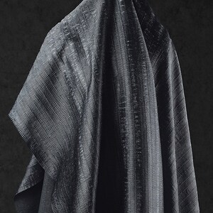 May include: A draped, dark gray fabric with a subtle, textured, ribbed pattern. The fabric is folded, creating shadows and highlights that emphasize the texture. The overall effect is one of depth and luxury.