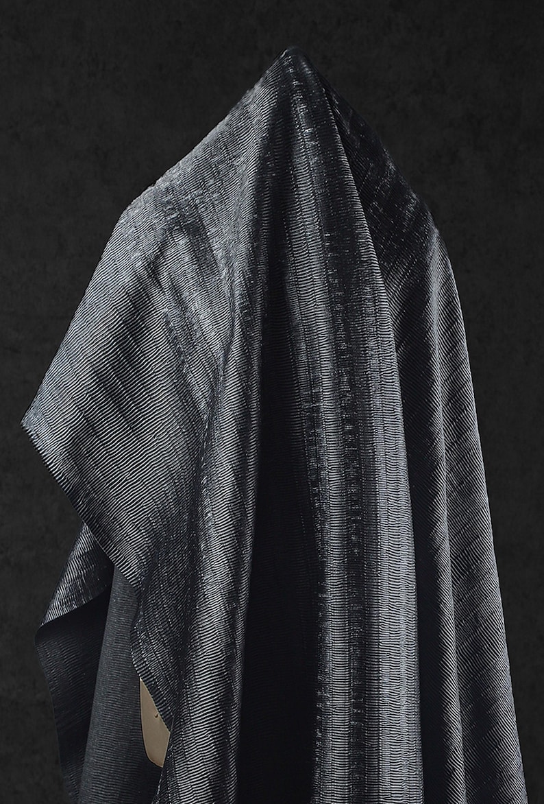 May include: A draped, dark gray fabric with a subtle, textured, ribbed pattern. The fabric is folded, creating shadows and highlights that emphasize the texture. The overall effect is one of depth and luxury.