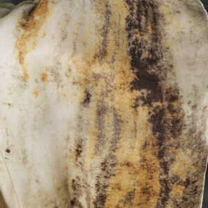 May include: Close-up of a fabric with a mottled pattern. The fabric has a cream-colored base with brown and tan streaks and blotches, creating a textured, organic appearance. The overall effect is reminiscent of animal hide.