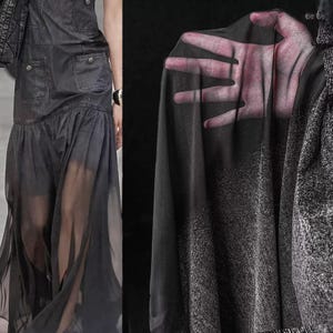 May include: A dark gray denim dress with pockets and a flowing, sheer skirt. The dress is paired with a black sheer fabric, and a textured gray jacket. The image showcases a fashion ensemble with a focus on texture and layering.