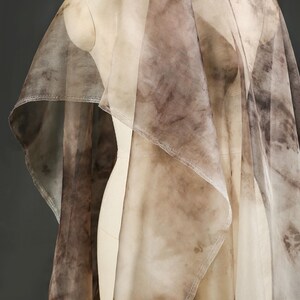 May include: A sheer, flowing fabric draped over a mannequin. The fabric features a mottled pattern in shades of brown and beige, creating a watercolor effect. The material appears lightweight and delicate, with visible seams.