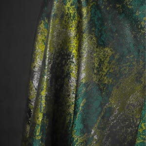 May include: Textured fabric with an abstract design in green, yellow, and silver. The material has a metallic sheen and a dark backdrop, creating a striking visual. Suitable for clothing or interior design.