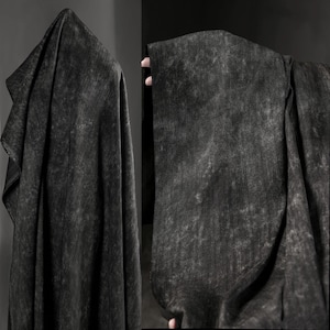 Può includere: Due sezioni di tessuto grigio scuro con un aspetto strutturato e screziato. Il tessuto è drappeggiato, creando pieghe e ombre. Il materiale ha un'estetica usurata e vintage, adatta all'abbigliamento o all'arredamento.