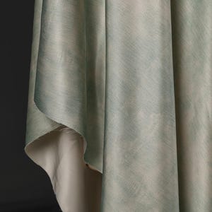 May include: Close-up of draped fabric with a watercolor effect. The fabric has a light green and blue color palette with a subtle texture. The underside of the fabric is a light beige color.
