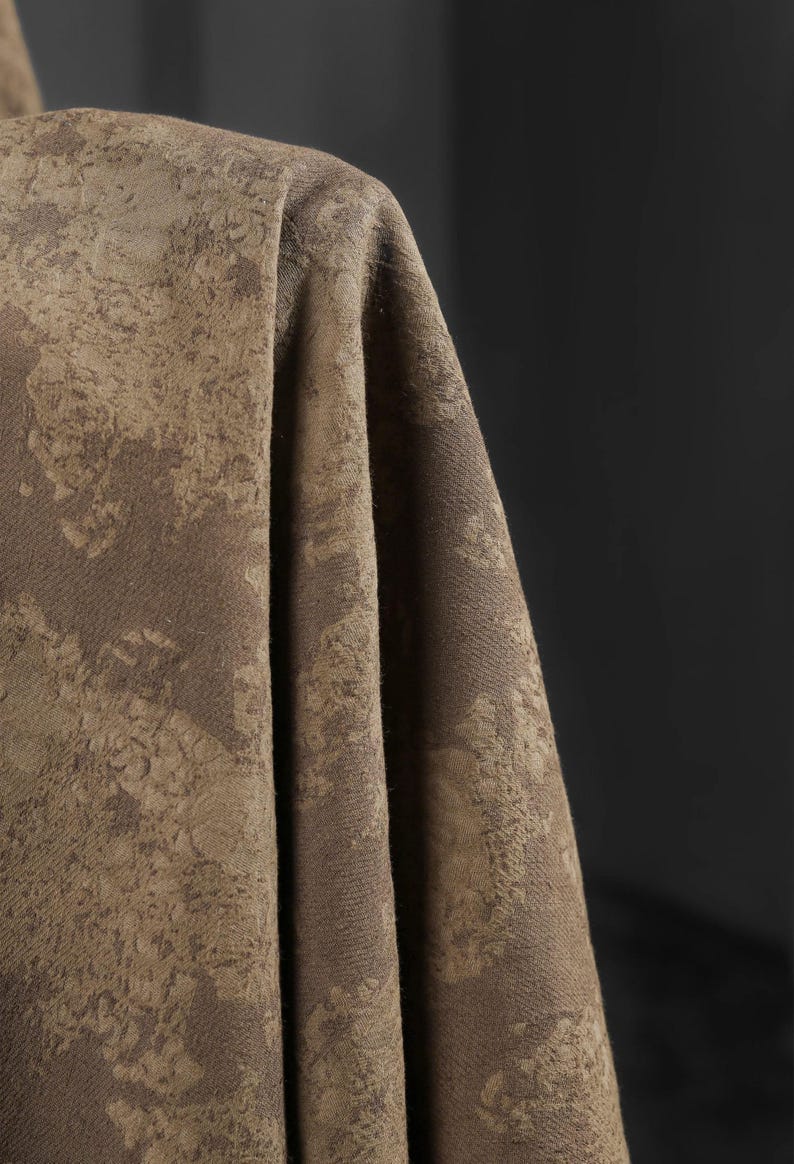 May include: Close-up of a draped fabric in shades of brown and tan. The textile has a textured, mottled pattern, with areas of lighter and darker tones creating a visual depth. The fabric appears to be thick and possibly suitable for upholstery or drapery.
