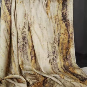 May include: A draped fabric with a cream-colored base and vertical streaks of brown and yellow. The fabric has a flowing, textured appearance, with darker brown spots scattered throughout the design. The overall effect is reminiscent of a natural, earthy pattern.