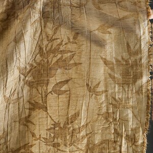 May include: Close-up of a beige fabric with a repeating pattern of brown leaves and stems. The fabric has a textured, pleated appearance and a frayed edge on the right side. The overall aesthetic is natural and organic.