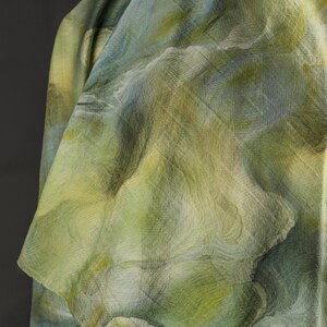 Puede incluir: Primer plano de una tela con un patr&oacute;n similar a la acuarela en tonos verdes, azules y amarillos. La tela tiene un aspecto texturizado con l&iacute;neas sutiles y un dise&ntilde;o fluido y org&aacute;nico. La tela est&aacute; drapeada, mostrando pliegues y sombras.