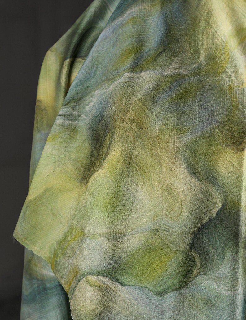 Puede incluir: Primer plano de una tela con un patr&oacute;n similar a la acuarela en tonos verdes, azules y amarillos. La tela tiene un aspecto texturizado con l&iacute;neas sutiles y un dise&ntilde;o fluido y org&aacute;nico. La tela est&aacute; drapeada, mostrando pliegues y sombras.