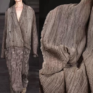 Pode incluir: Um blazer castanho texturizado com um design de abotoamento duplo e decote em V. O blazer é combinado com calças a condizer com um padrão floral. O tecido tem uma textura de riscas verticais. O visual geral é um conjunto monocromático.