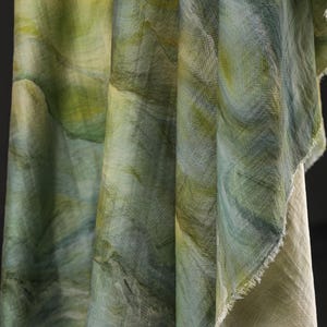 Puede incluir: Primer plano de tela drapeada con un patr&oacute;n similar a la acuarela en tonos verdes y azules. La tela tiene un aspecto texturizado con pinceladas visibles y un borde sin rematar. El efecto general es suave y fluido, lo que sugiere un textil.