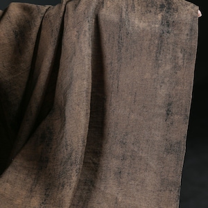 Puede incluir: Un textil drapeado en tonos marrones con acentos oscuros y texturizados. La tela tiene una apariencia desgastada, con un sutil patr&oacute;n tejido visible. El efecto general es de un material r&uacute;stico y envejecido.