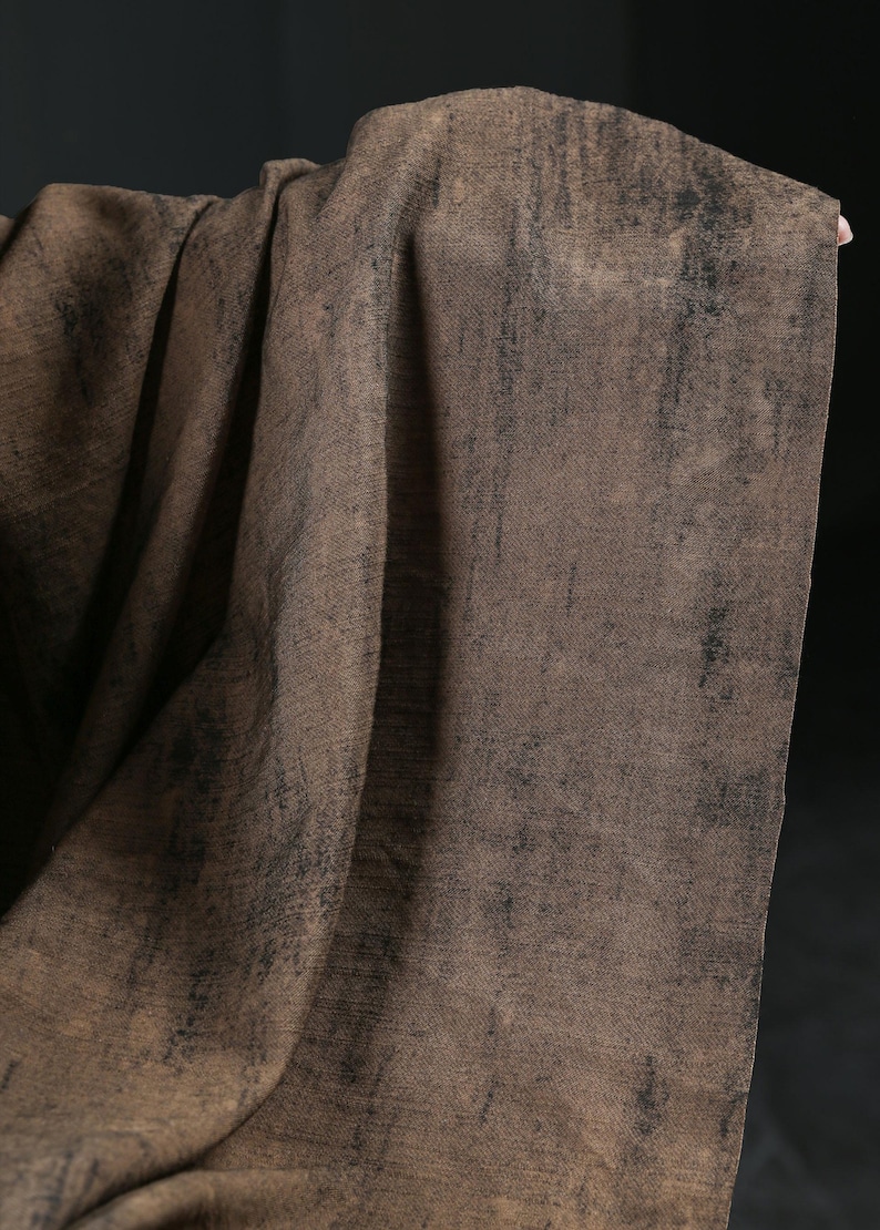 Puede incluir: Un textil drapeado en tonos marrones con acentos oscuros y texturizados. La tela tiene una apariencia desgastada, con un sutil patr&oacute;n tejido visible. El efecto general es de un material r&uacute;stico y envejecido.