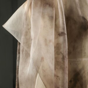 May include: A sheer, cream-colored fabric with brown, mottled patterns draped over a dress form. The fabric is lightweight and appears to be silk or a similar material. The design suggests a focus on textile art or fashion.