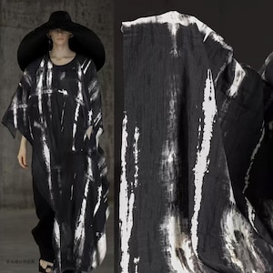 Peut inclure: Robe noire et blanche à motifs et chapeau à larges bords assorti. La robe présente un design ample et fluide avec des motifs verticaux blancs en forme de coups de pinceau sur fond noir. Le tissu semble léger et drapé.