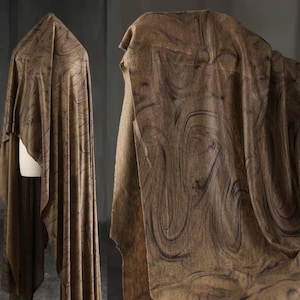 May include: Brown fabric with a swirling, marbled pattern. The fabric is draped over a form, showcasing its texture and flow. The design features dark brown lines against a lighter brown background, creating a visual depth. This textile is suitable for apparel or home decor.