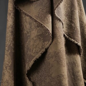 May include: Close-up of a draped fabric with a textured, mottled pattern in shades of brown and tan. The edges of the fabric are frayed, adding a rustic touch. The material appears to be heavy, suitable for upholstery or drapery.