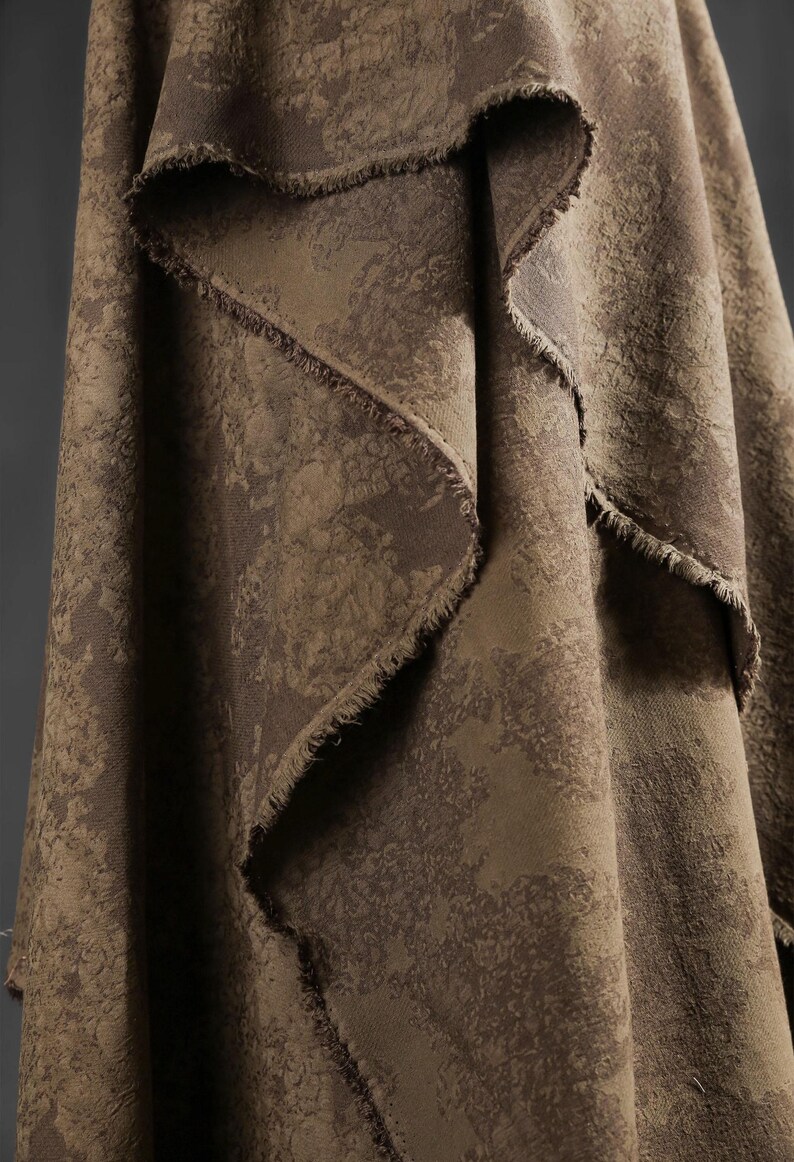 May include: Close-up of a draped fabric with a textured, mottled pattern in shades of brown and tan. The edges of the fabric are frayed, adding a rustic touch. The material appears to be heavy, suitable for upholstery or drapery.