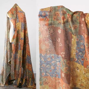 May include: Patchwork fabric featuring a floral design in orange, blue, yellow, and brown hues. The material is draped over a mannequin. The fabric is lightweight and suitable for sewing projects. The background is white.
