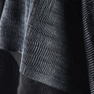 May include: Close-up of a textured, dark gray fabric with a ribbed pattern. The fabric appears to be draped, with folds and shadows adding depth. The surface has a subtle sheen, enhancing the visual texture.