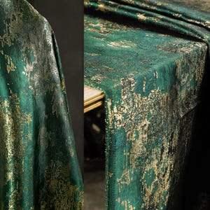 Può includere: Tessuto verde smeraldo con rivestimento metallico dorato. Il tessuto ha un aspetto strutturato, con gli accenti dorati che creano un effetto artistico invecchiato. Il tessuto è drappeggiato, suggerendo che potrebbe essere utilizzato per tende o una tovaglia.
