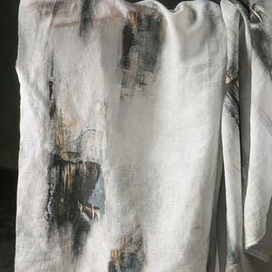 May include: White linen fabric with an abstract design featuring dark grey, brown, and teal brushstrokes. The fabric is draped, showcasing the textured pattern and colour variations.