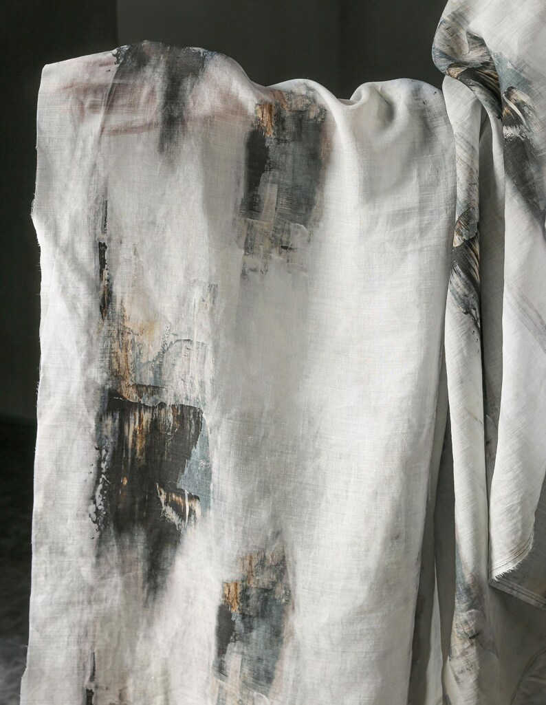 May include: White linen fabric with an abstract design featuring dark grey, brown, and teal brushstrokes. The fabric is draped, showcasing the textured pattern and colour variations.