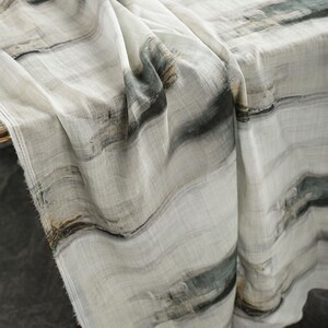 May include: A draped fabric with an abstract pattern in white, grey, and muted green. The design features flowing, wave-like lines, creating a textured appearance. The fabric is likely linen or a similar lightweight material, suitable for home decor.