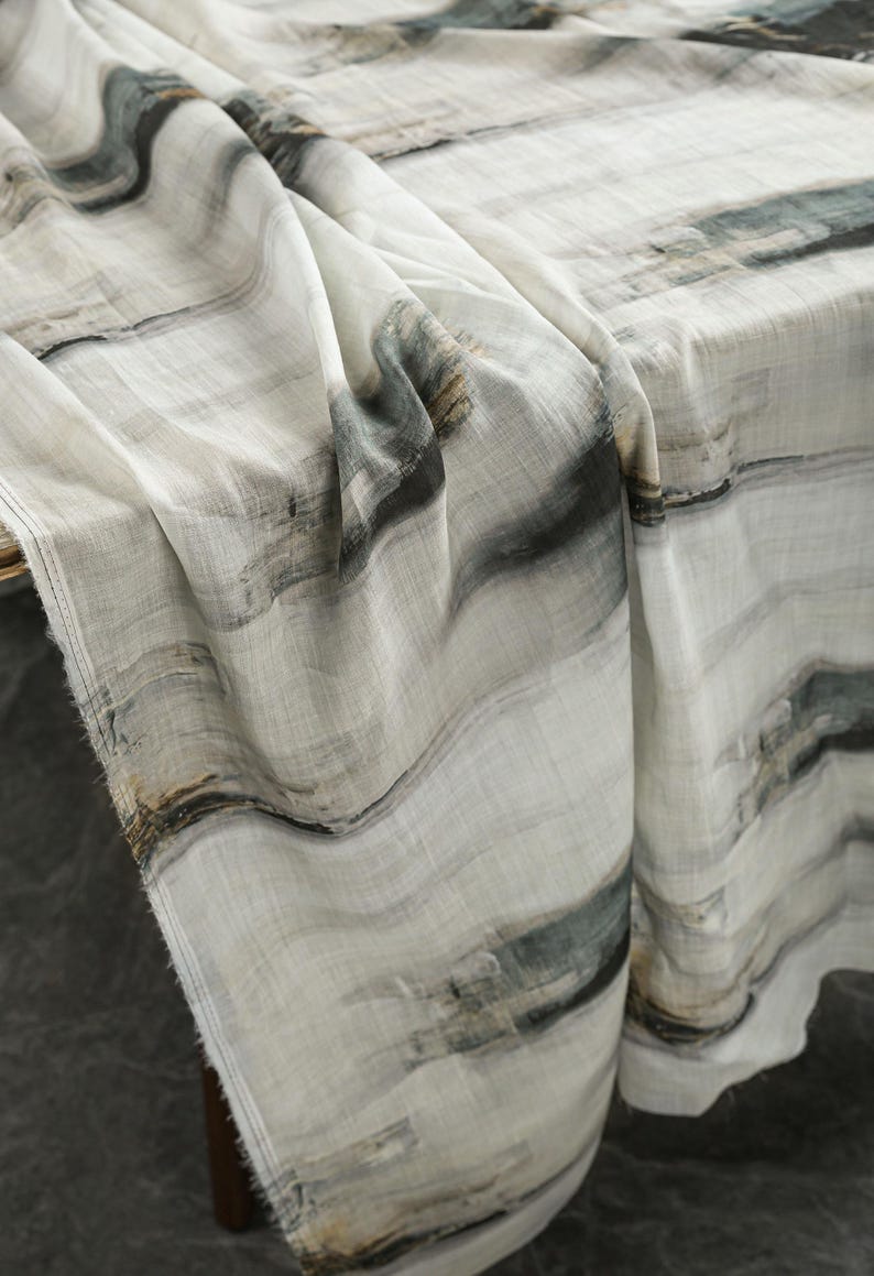 May include: A draped fabric with an abstract pattern in white, grey, and muted green. The design features flowing, wave-like lines, creating a textured appearance. The fabric is likely linen or a similar lightweight material, suitable for home decor.