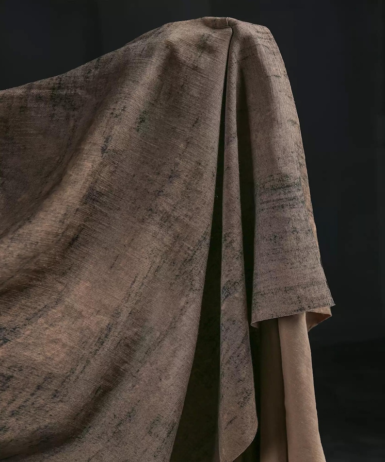 Puede incluir: Una tela drapeada en tonos marrones y beige, con una apariencia texturizada y desgastada. La tela tiene marcas lineales oscuras, creando una est&eacute;tica art&iacute;stica y desgastada. Los pliegues y las sombras a&ntilde;aden profundidad al textil.