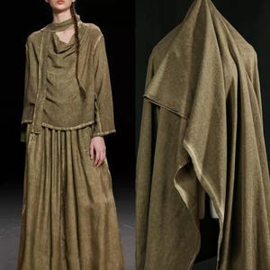 May include: Olive green two-piece outfit with a long-sleeved top and a long skirt. The top has a cowl neck and a matching scarf. The fabric has a textured appearance. A large piece of olive green fabric is draped in the background.