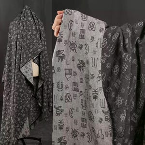 May include: Gray fabric with a repeating pattern of white symbols. The fabric is draped over a mannequin and held by a hand, showcasing the design and texture. The fabric appears to be a medium weight material.