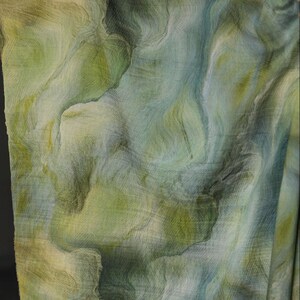 Puede incluir: Primer plano de una tela con un patr&oacute;n fluido similar a una acuarela. La tela presenta tonos de verde, azul y amarillo, creando un efecto veteado. El material parece ligero y fluido, adecuado para ropa o decoraci&oacute;n del hogar.