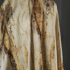 May include: A draped fabric with a marbled pattern. The fabric features a blend of beige, brown, and gold tones, creating a natural, organic aesthetic. The material appears soft and flowing, with visible folds and textures.