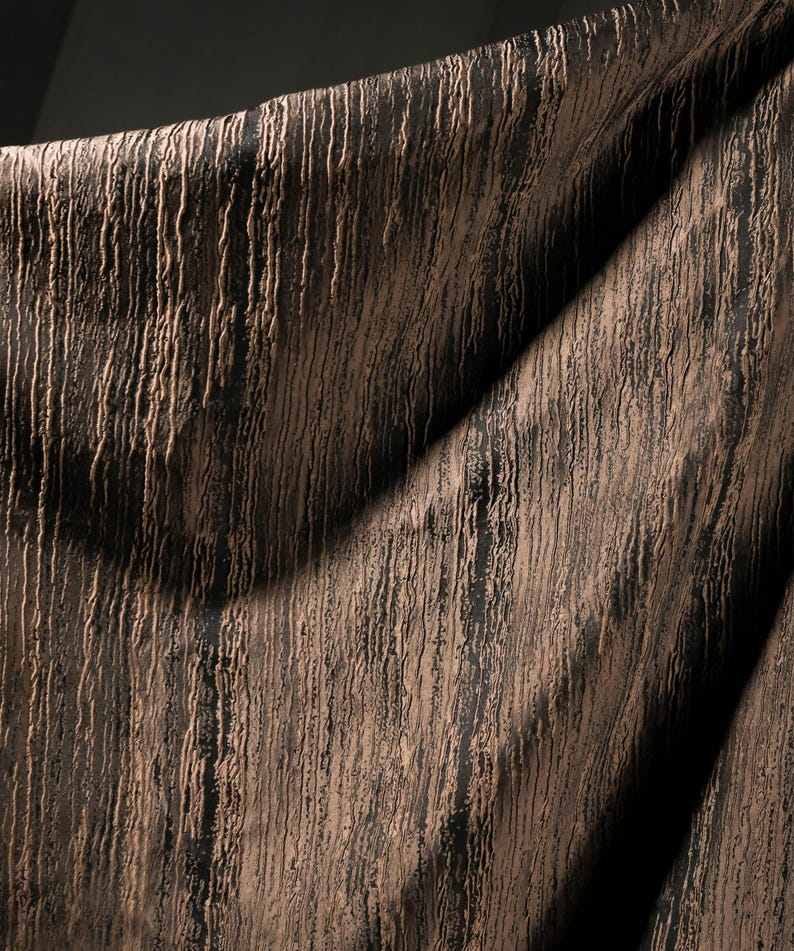 May include: Close-up of a textured fabric with a vertical, linear pattern. The fabric has a dark brown base color with lighter brown, raised lines running from top to bottom. The fabric is draped, creating shadows and highlights.