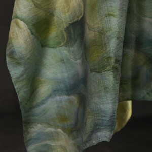 Puede incluir: Una tela fluida con un dise&ntilde;o similar a una acuarela en tonos verdes, azules y amarillos. El material parece ligero y tiene una superficie texturizada. La tela est&aacute; drapeada, mostrando el patr&oacute;n y las variaciones de color.