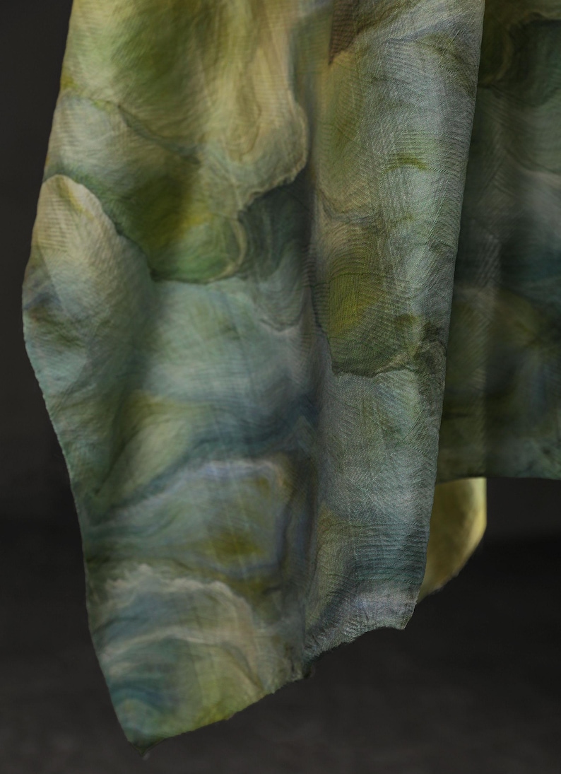 Puede incluir: Una tela fluida con un dise&ntilde;o similar a una acuarela en tonos verdes, azules y amarillos. El material parece ligero y tiene una superficie texturizada. La tela est&aacute; drapeada, mostrando el patr&oacute;n y las variaciones de color.