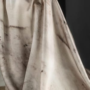 May include: Off-white fabric with dark brown and black mottled patterns. The fabric is draped, showing folds and textures. The overall effect is a blend of light and dark tones, creating a visual contrast. The fabric appears to be lightweight and flowing.
