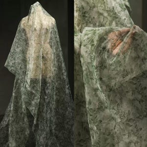 Könnte beinhalten: Transparenter Stoff mit einem grün-weißen Blumenmuster, drapiert über einer Schaufensterpuppe. Der Stoff ist durchscheinend und zeigt die Form darunter. Das Muster zeigt ein zartes Blattdesign und erzeugt eine weiche, luftige Ästhetik. Geeignet für Kleidung oder Heimdekoration.