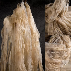 Puede incluir: Primer plano de tela beige y transparente, arrugada y colgada. La tela parece ligera y delicada. La imagen resalta la textura y el movimiento del material.