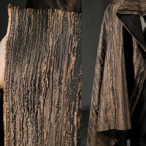 Puede incluir: Tejido texturizado con un patrón similar a la corteza, en tonos marrón y negro. La tela está drapeada, posiblemente parte de un abrigo o chaqueta, con un cuello y solapas visibles.