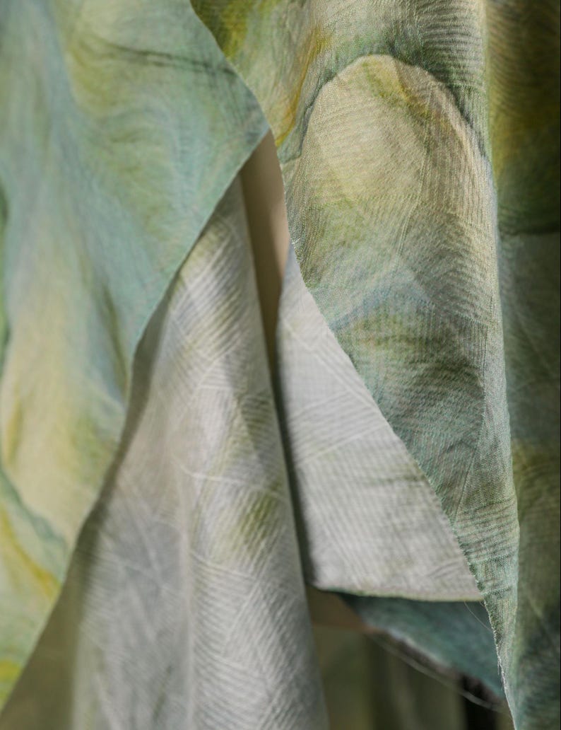 Puede incluir: Primer plano de tela fluida en tonos verdes, amarillos y azules. El material parece ligero, con un patr&oacute;n sutil visible en los pliegues. La tela est&aacute; en capas, creando profundidad y textura, lo que sugiere una bufanda o chal.