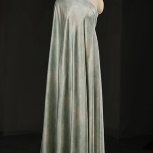 May include: A draped fabric in shades of pale blue and green is displayed on a mannequin. The fabric has a soft, watercolor-like appearance, with subtle variations in color. The material is draped to create a flowing effect, suggesting it is suitable for apparel or home decor.