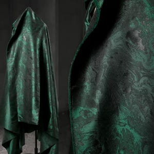 May include: Emerald green fabric with a marbled pattern, draped over a stand. The fabric has a glossy sheen and a dark, swirling design. The fabric is a rich, dark green color.