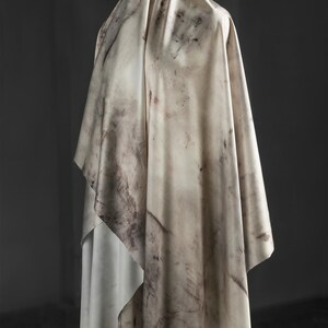 May include: A draped fabric with a marbled pattern in shades of cream, beige, and brown. The fabric is draped over an unseen form, creating folds and shadows. The overall effect is soft and textured, with a natural, organic feel.