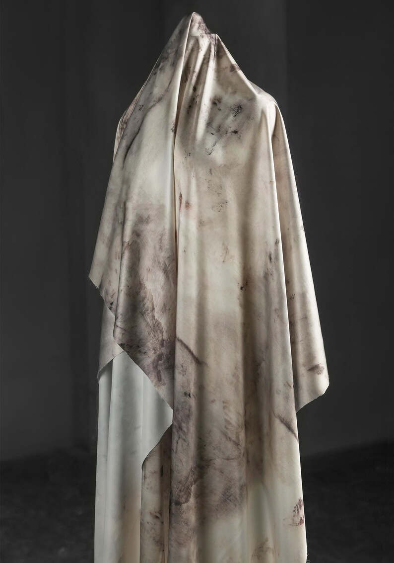 May include: A draped fabric with a marbled pattern in shades of cream, beige, and brown. The fabric is draped over an unseen form, creating folds and shadows. The overall effect is soft and textured, with a natural, organic feel.