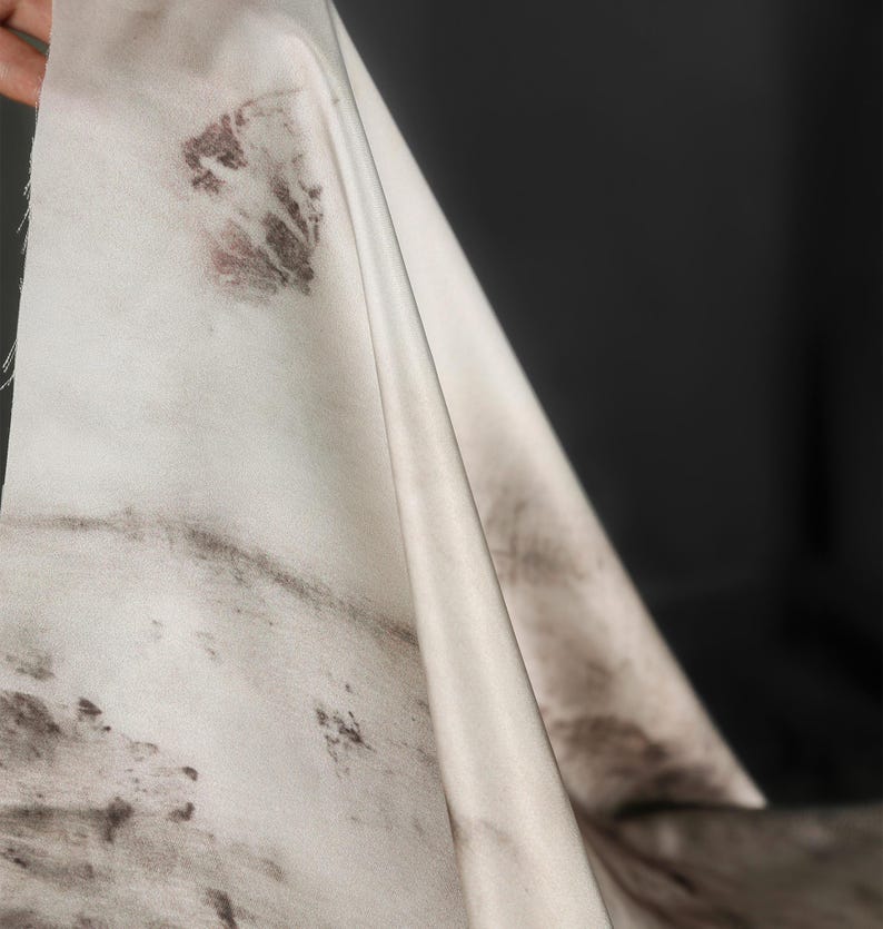 May include: Off-white fabric with dark brown and maroon botanical prints. The fabric is draped, revealing folds and textures. The dark background contrasts with the light fabric, highlighting the organic patterns.
