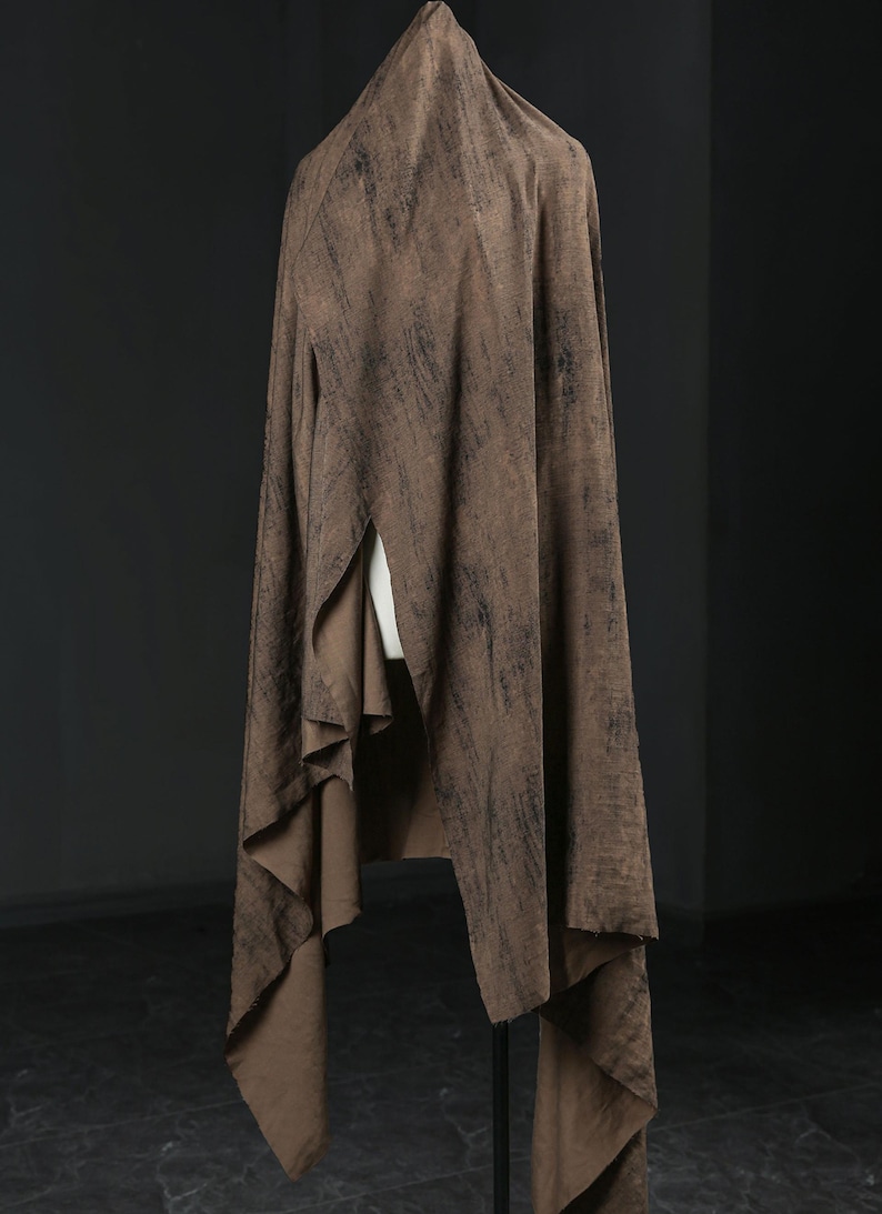 Puede incluir: Una tela marr&oacute;n drapeada sobre un maniqu&iacute;, que muestra un patr&oacute;n texturizado y moteado. El dise&ntilde;o de la tela es fluido, con un tono c&aacute;lido y terroso y acentos m&aacute;s oscuros. Ideal para ropa o textiles.