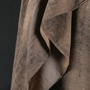 Puede incluir: Primer plano de una tela marr&oacute;n drapeada con textura. El material presenta pliegues en capas y un brillo sutil. Los patrones m&aacute;s oscuros y moteados crean profundidad, sugiriendo un textil de fibra natural. El dise&ntilde;o es intrincado y atractivo.